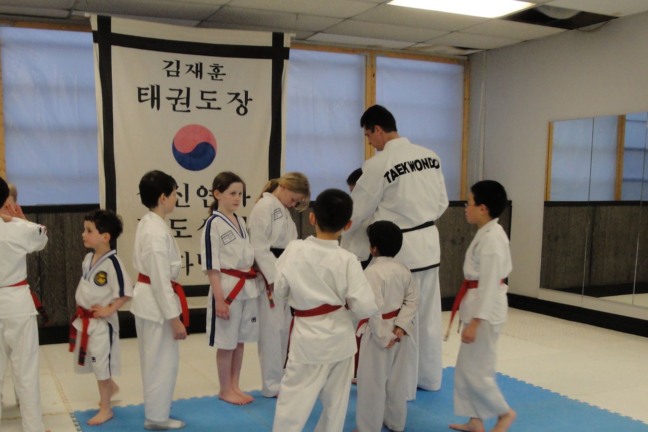 Michael O&rsquo;Malley on the floor with a children&rsquo;s class at the Jae Hun Kim Taekwon-Do Institute in Boston, beneath the school&rsquo;s Korean banner.